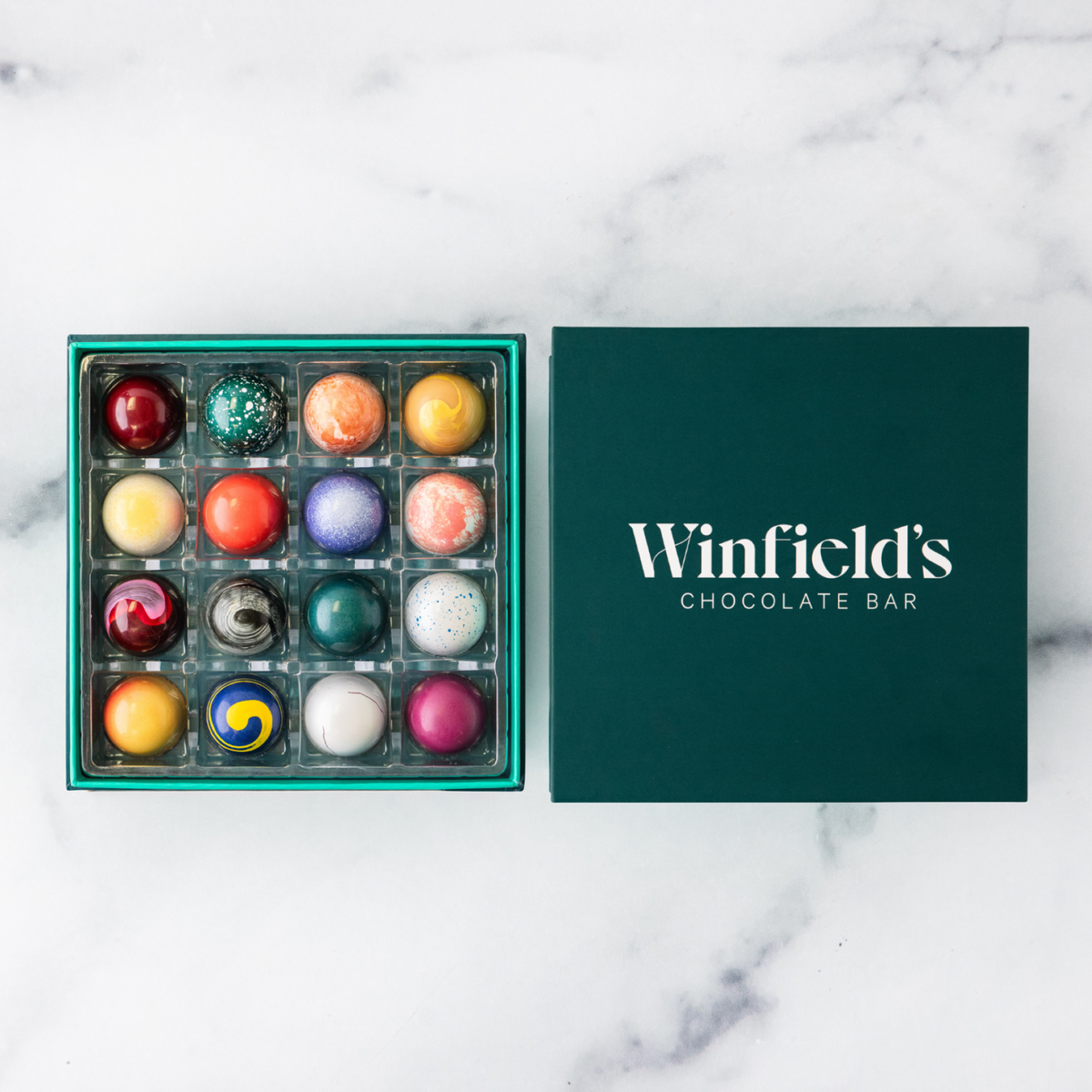 Winfield's Signature Truffle Collection 16-piece box open from above, teal tray beside the dark green lid