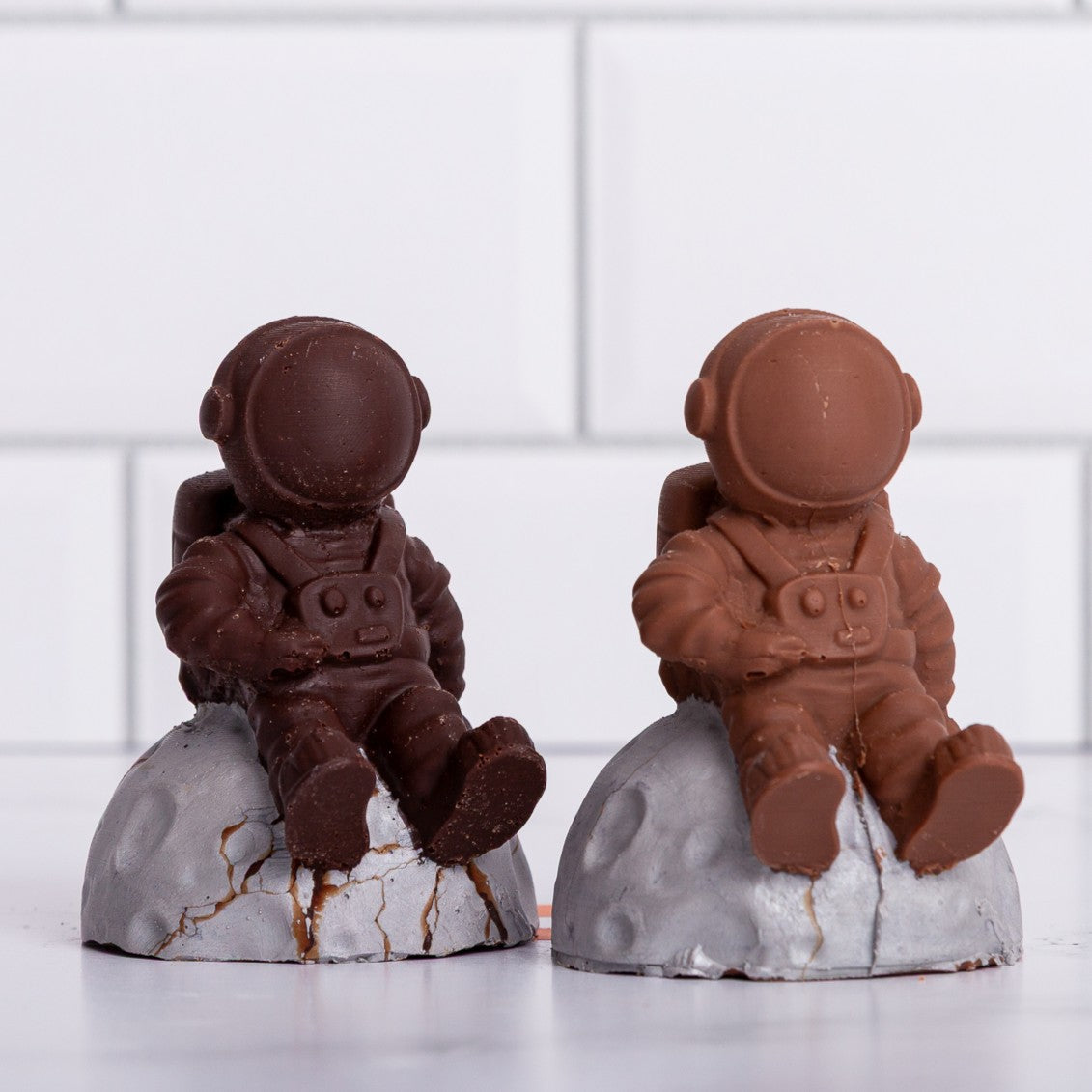Two Winfield's molded chocolate astronauts seated on textured moon-rock bases