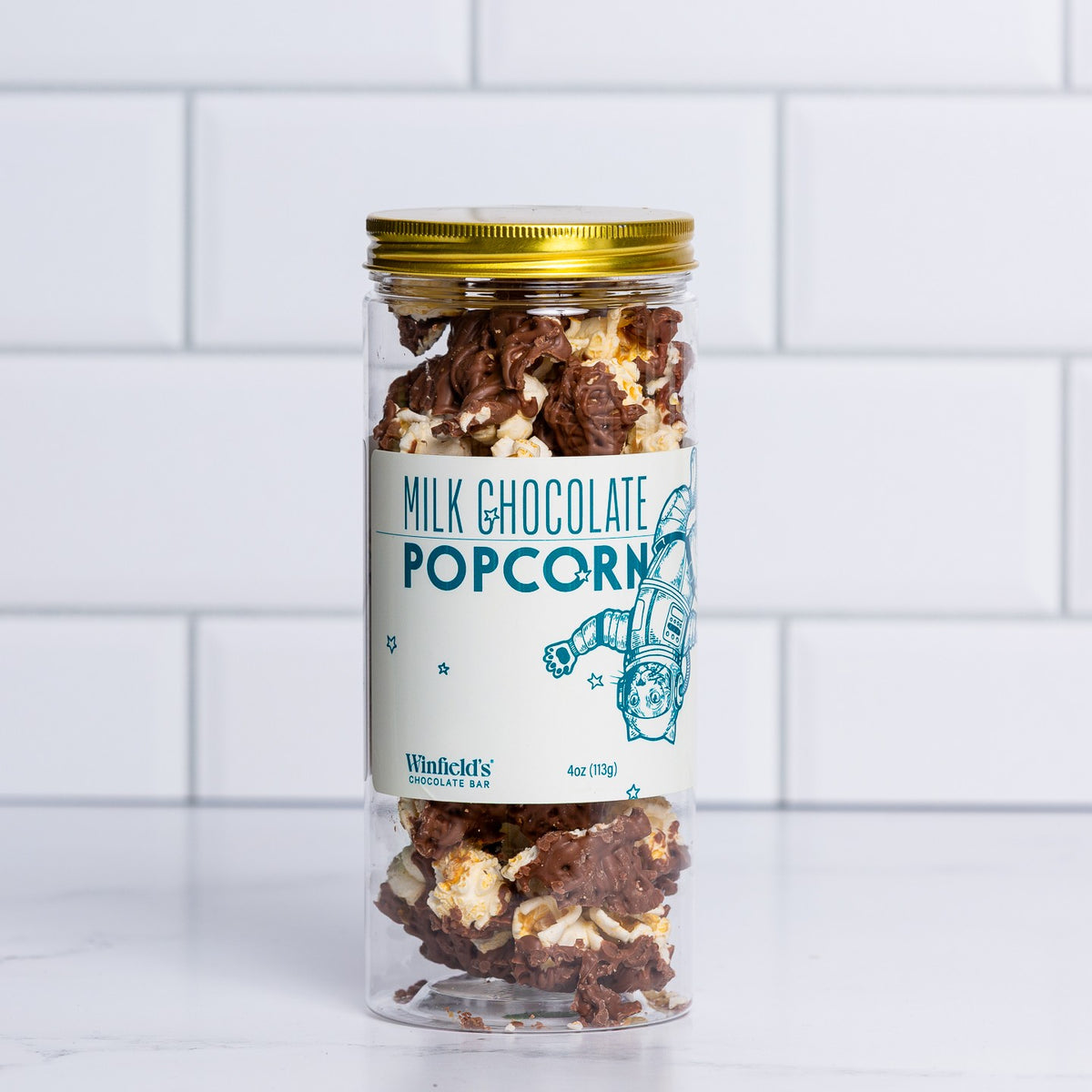 Tall glass jar with a gold lid filled with Winfield's Milk Chocolate Popcorn