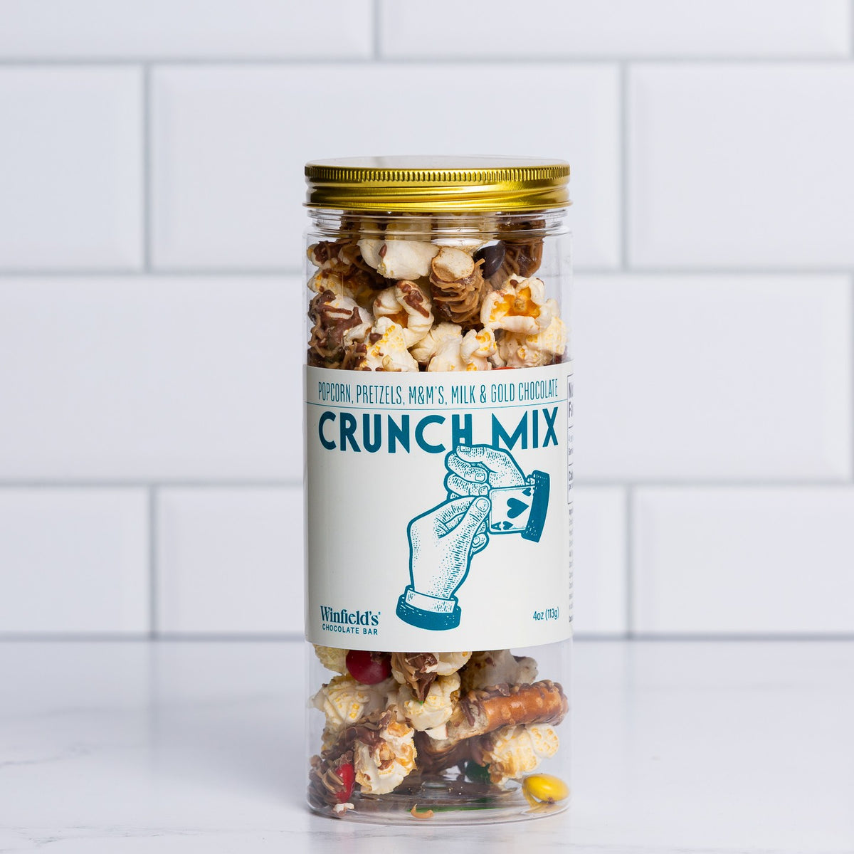 Tall glass jar with a gold lid filled with Winfield's Crunch Mix
