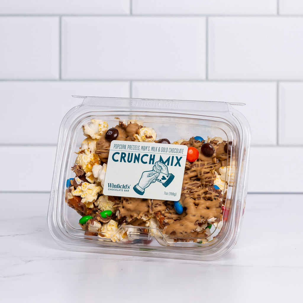 Clear tub of Winfield's Crunch Mix with chocolate-coated pretzels, popcorn and candy-shell pieces