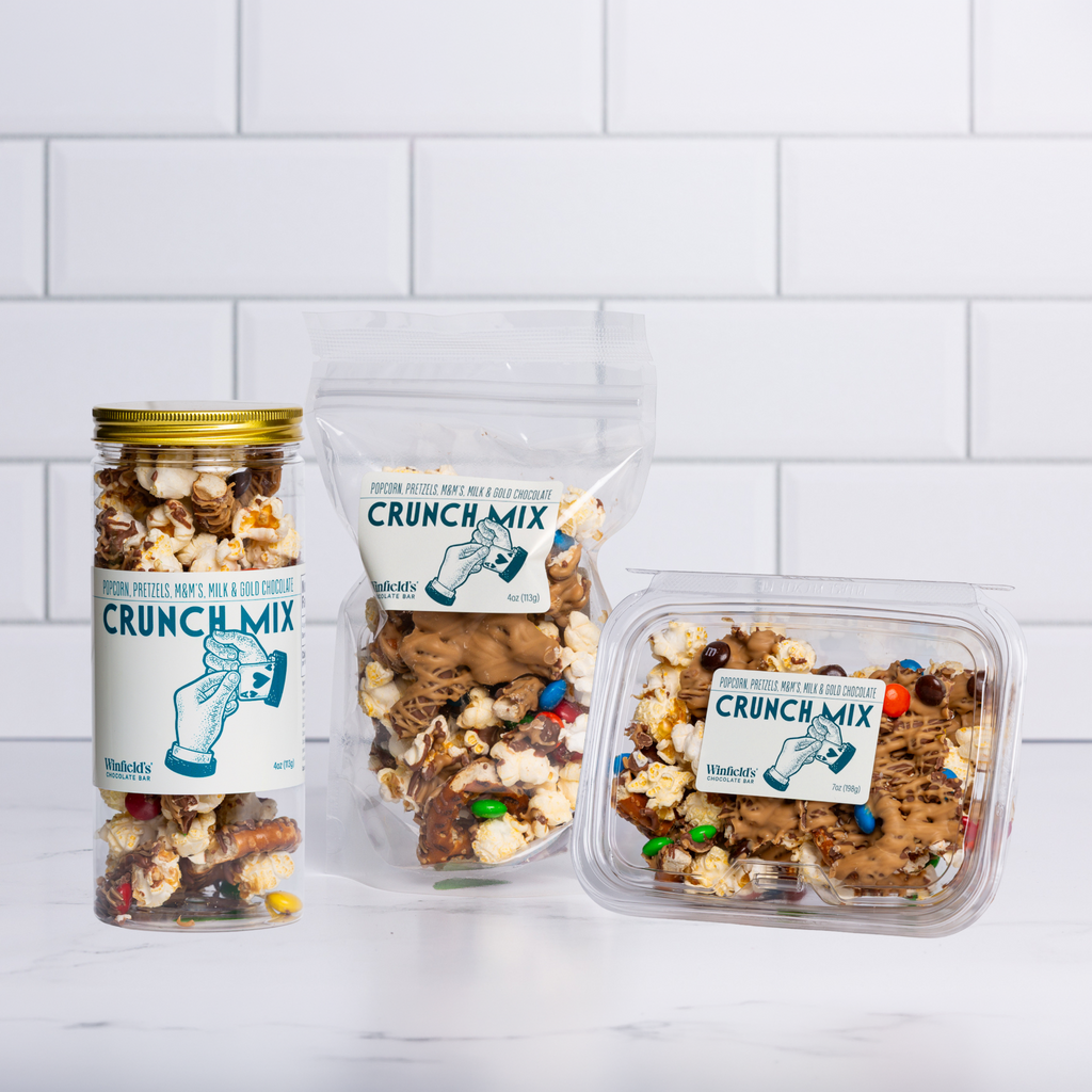 The Winfield's Crunch Mix range — glass jar, stand-up pouch and clear tub — on a marble counter