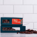 Winfield's Dark Chocolate Spicy Texas Pecans in stacked teal window boxes with loose pieces alongside
