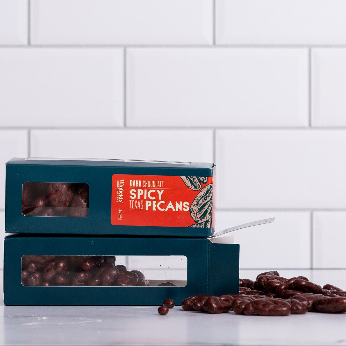 Winfield's Dark Chocolate Spicy Texas Pecans in stacked teal window boxes with loose pieces alongside