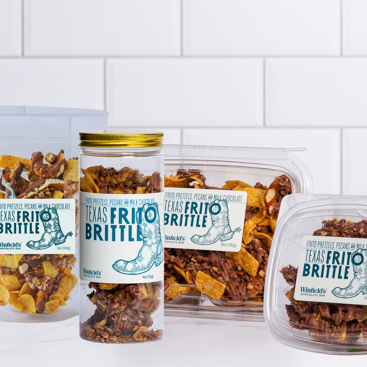 The Winfield's Texas Frito Brittle range — glass jar, clear tubs and pouch — on a marble counter