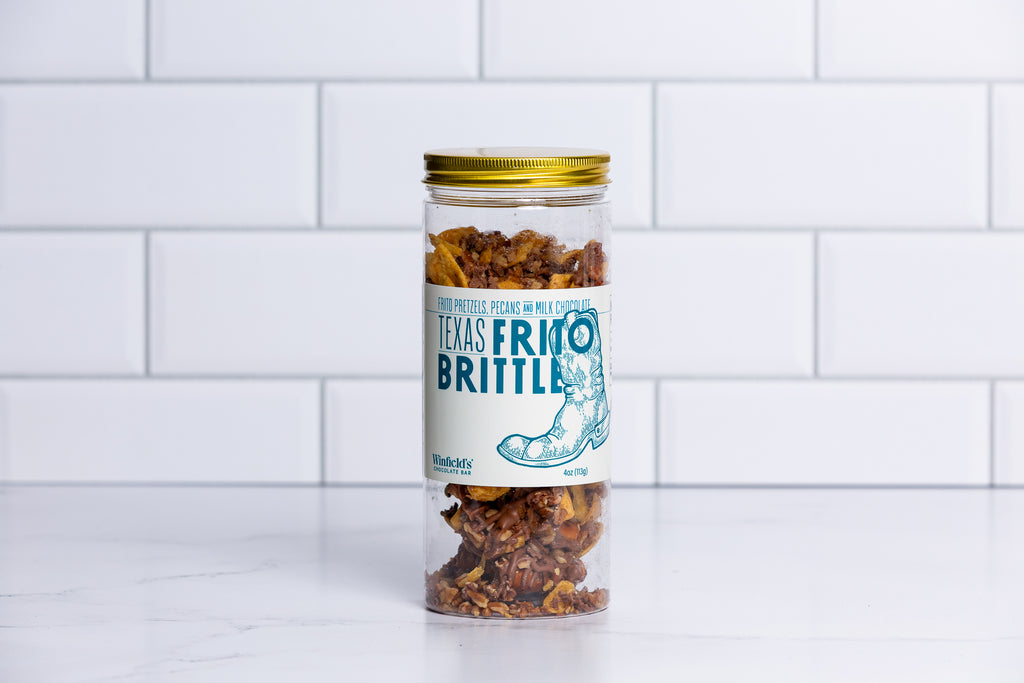 Tall glass jar with a gold lid filled with Winfield's Texas Frito Brittle