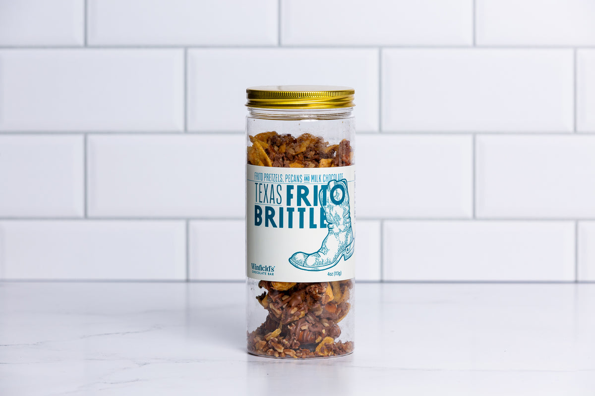 Tall glass jar with a gold lid filled with Winfield's Texas Frito Brittle