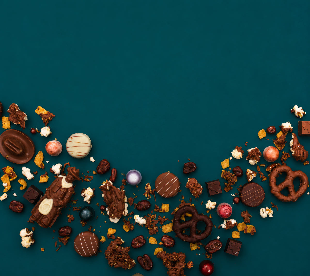 Winfield's truffles, chocolate-covered pretzels, popcorn and toffee scattered in a wide arc across a deep teal background