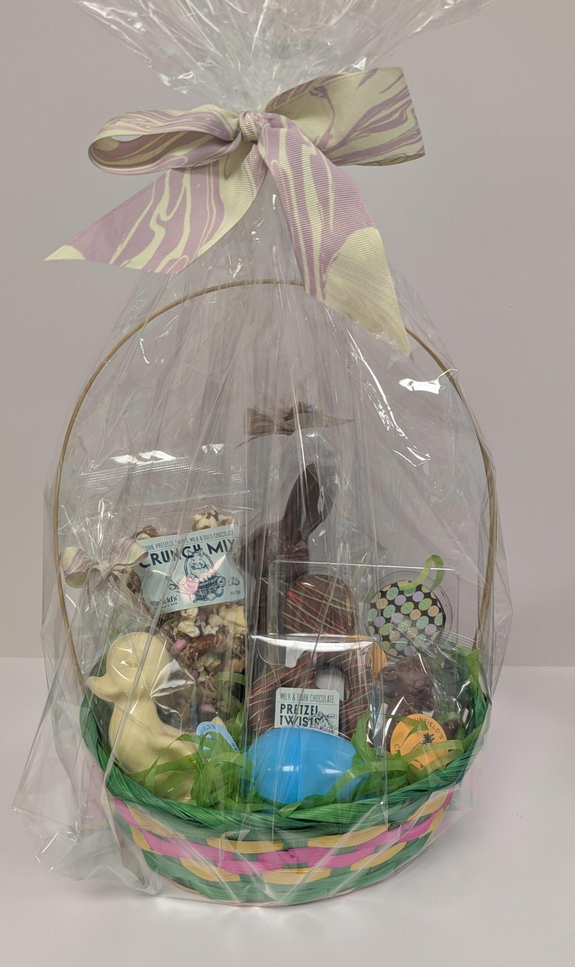 An Easter basket wrapped in cellophane and tied with pastel ribbon, filled with chocolate eggs, bunnies and pastel grass