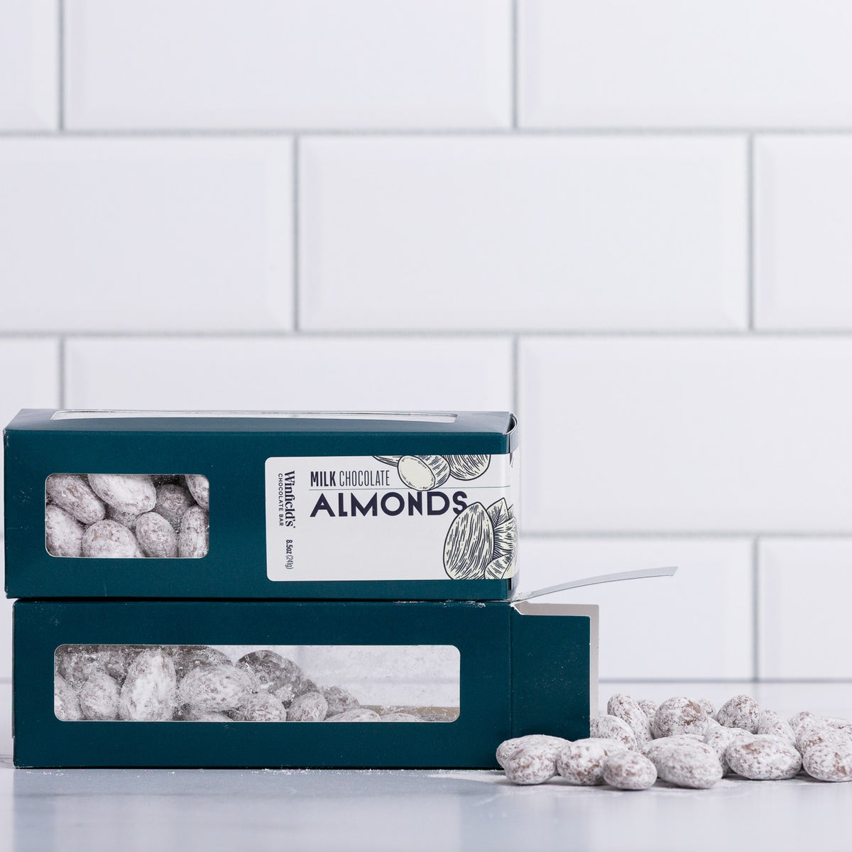 Winfield's Milk Chocolate Almonds in stacked teal window boxes with loose sugar-dusted almonds alongside