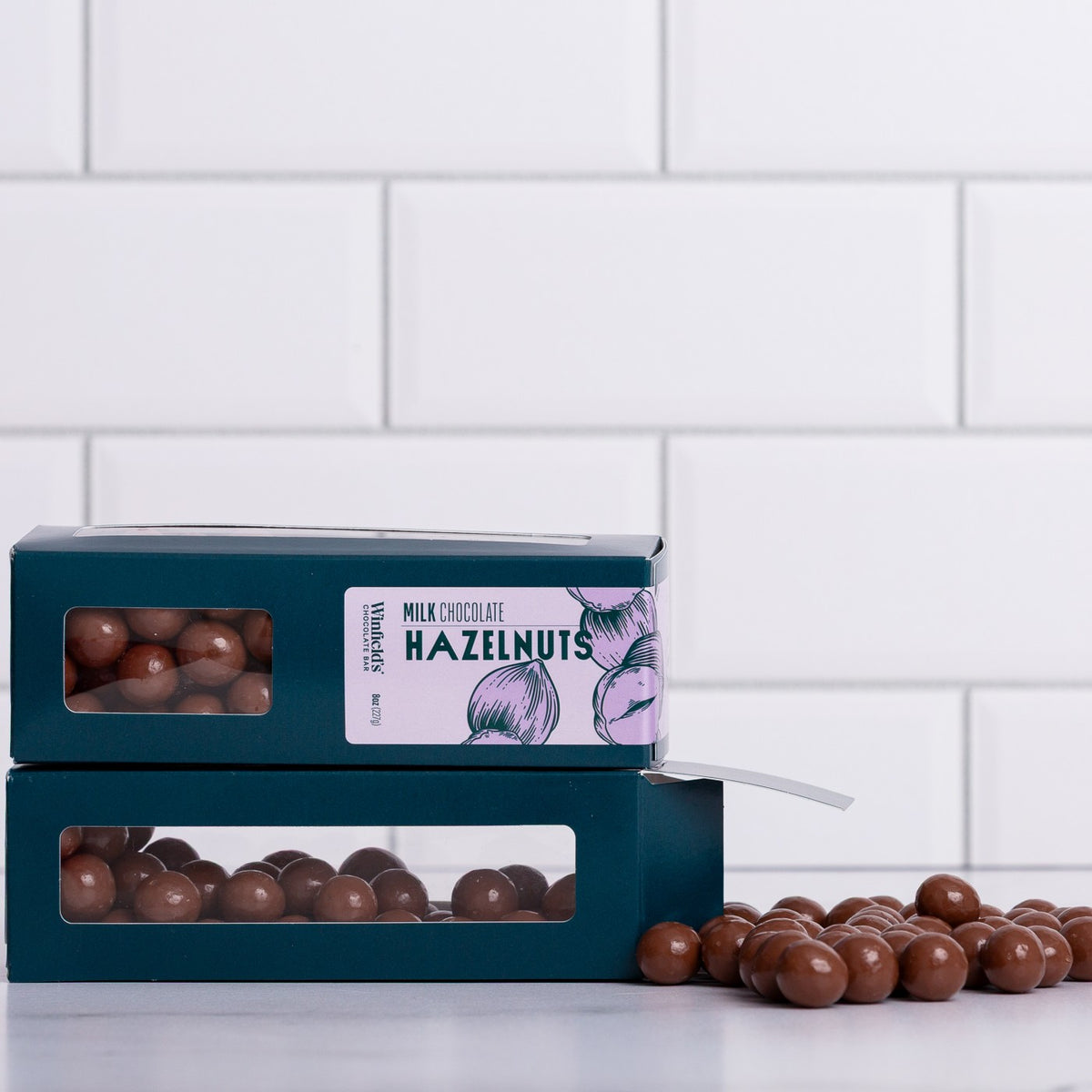 Winfield's Milk Chocolate Hazelnuts in stacked teal window boxes with loose pieces spilling out