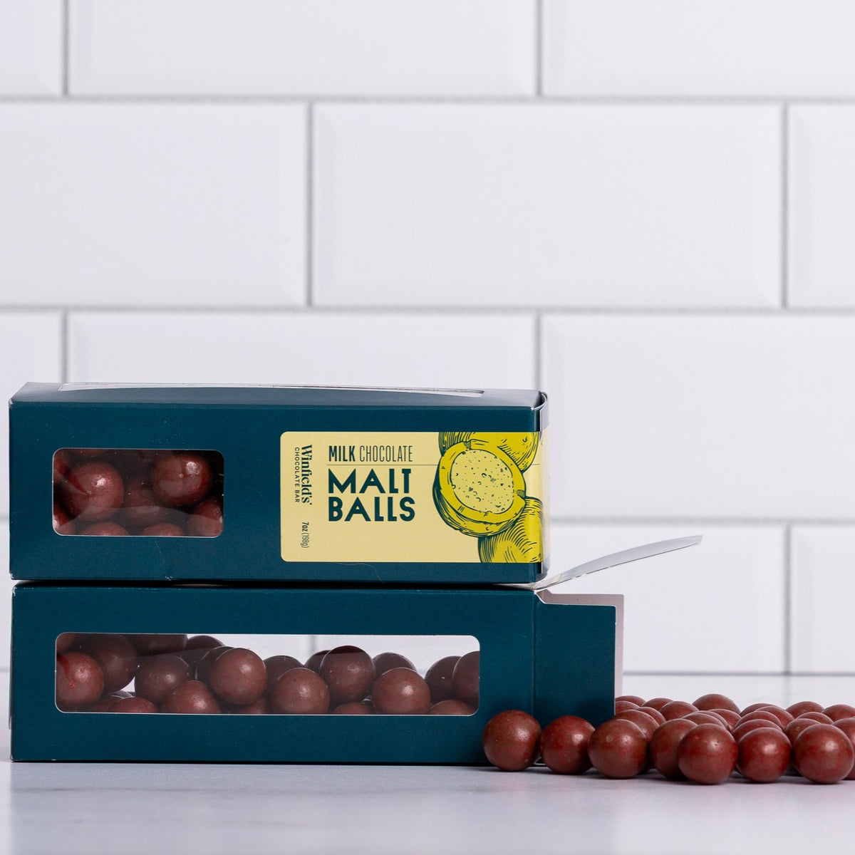Winfield's Milk Chocolate Malt Balls in stacked teal window boxes with loose malt balls alongside