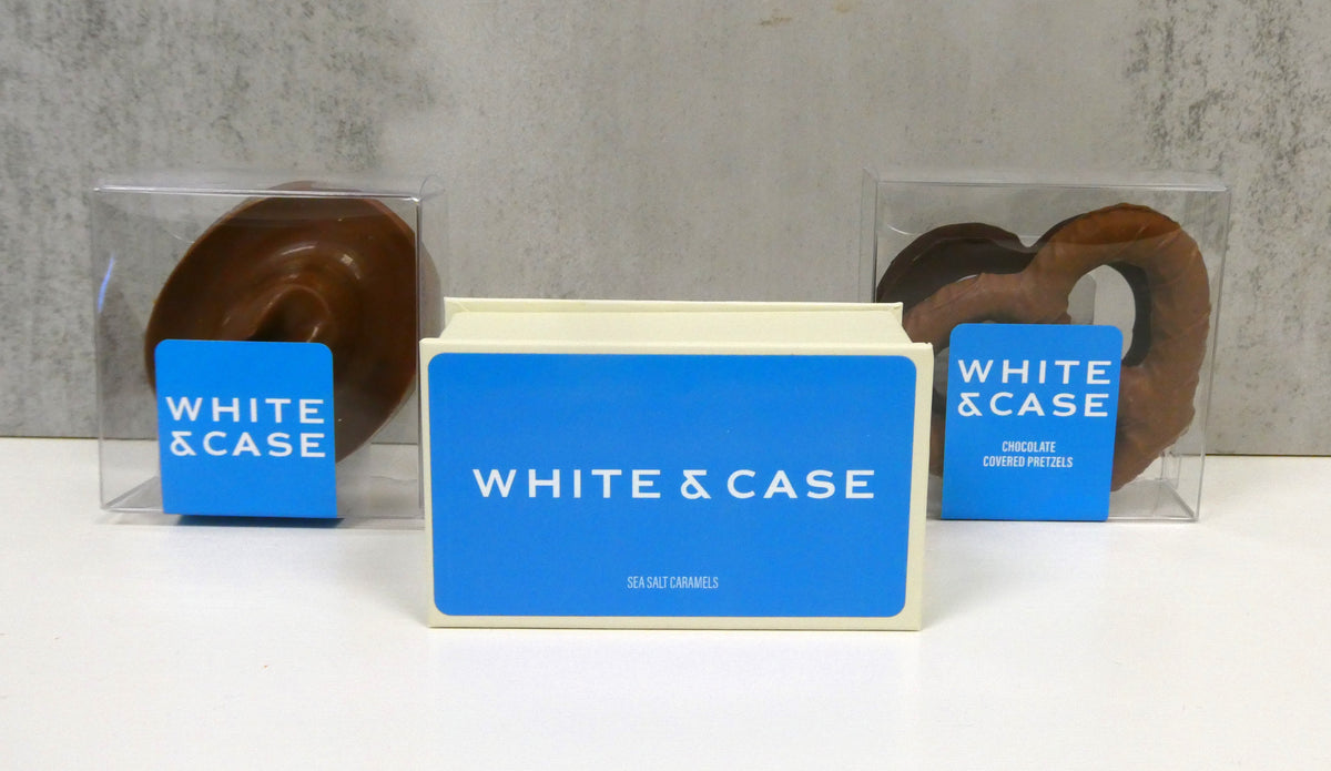 A White & Case branded gift box with chocolate-covered pretzels in clear window boxes