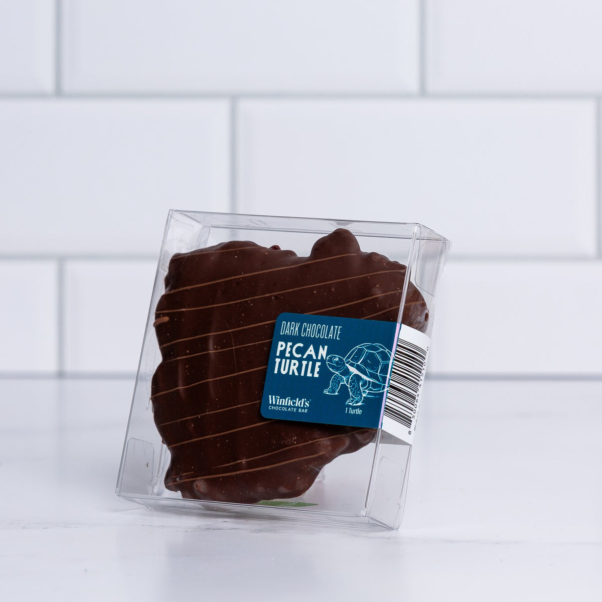 A single Winfield's dark chocolate pecan turtle in a clear gift box
