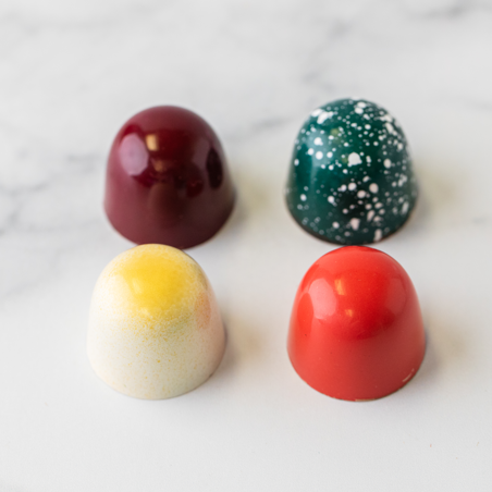 Four Winfield's signature truffles — deep red, speckled green, cream-and-yellow, and bright red — on marble