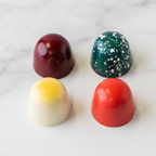 Four Winfield's signature truffles — deep red, speckled green, cream-and-yellow, and bright red — on marble