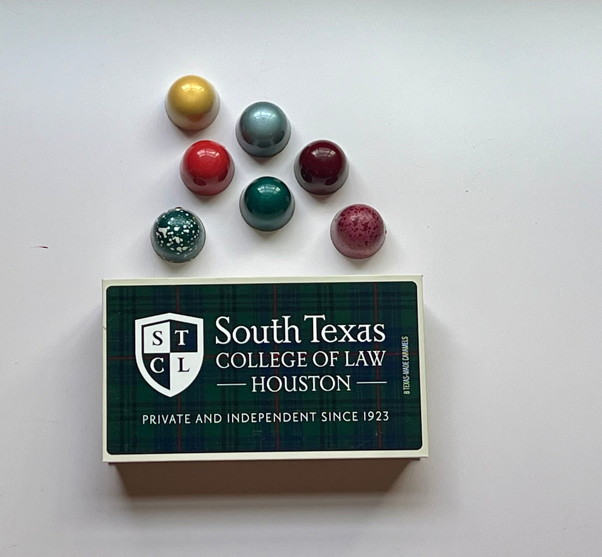 A South Texas College of Law Houston branded gift box topped with six hand-painted metallic truffles