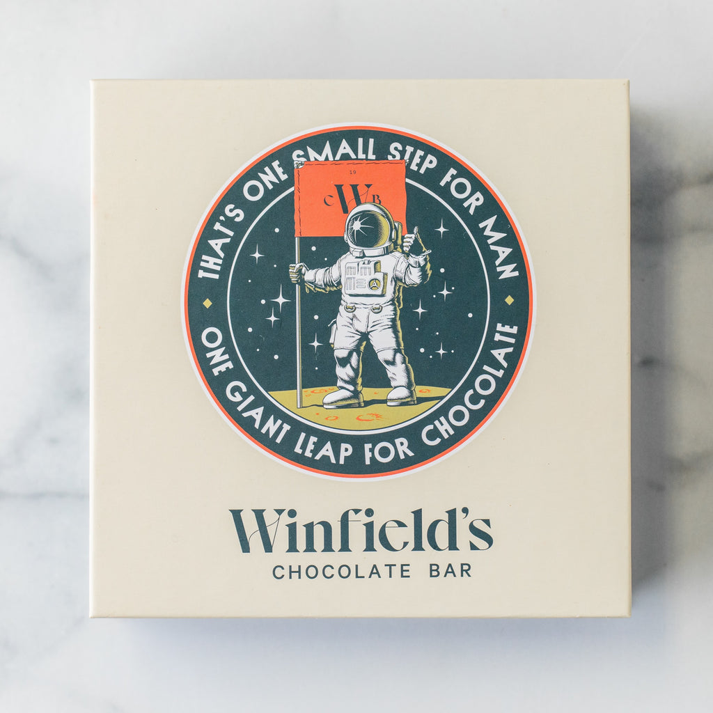 Cream Space City box lid with the Winfield's astronaut crest reading “That's one small step for man, one giant leap for chocolate”