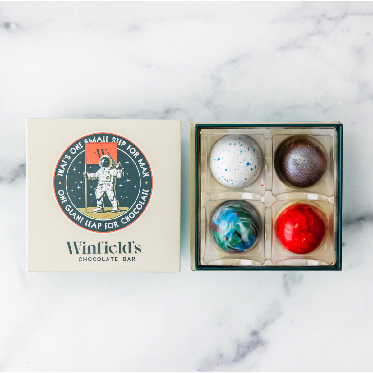 Winfield's Space City Truffle Collection 4-piece box open on marble beside the cream astronaut lid
