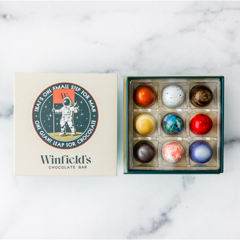 Winfield's Space City Truffle Collection 9-piece box open on marble beside the cream astronaut lid