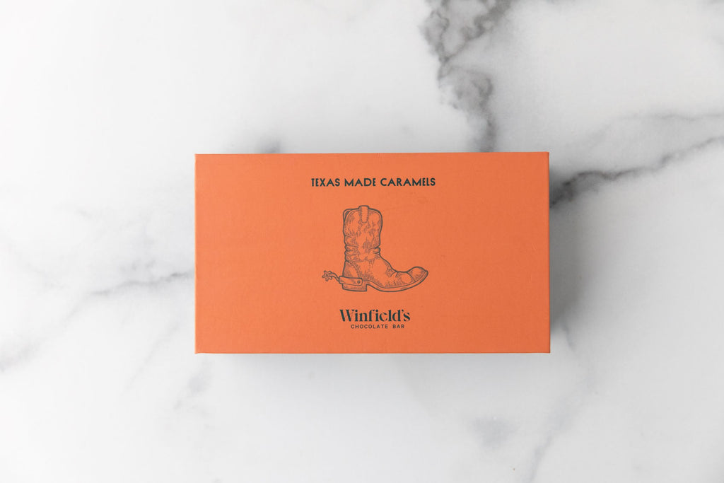 Closed orange Winfield's Texas-Made Caramels box with the cowboy-boot crest, on marble