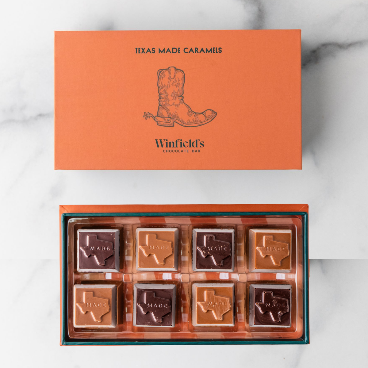 Winfield's Texas-Made Caramels 8-piece box open on marble, orange sleeve above a tray of Texas-shaped caramels