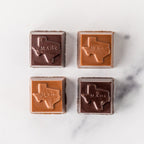 Four Winfield's Texas-Made Caramels in milk and dark chocolate, each embossed with the outline of Texas, on marble