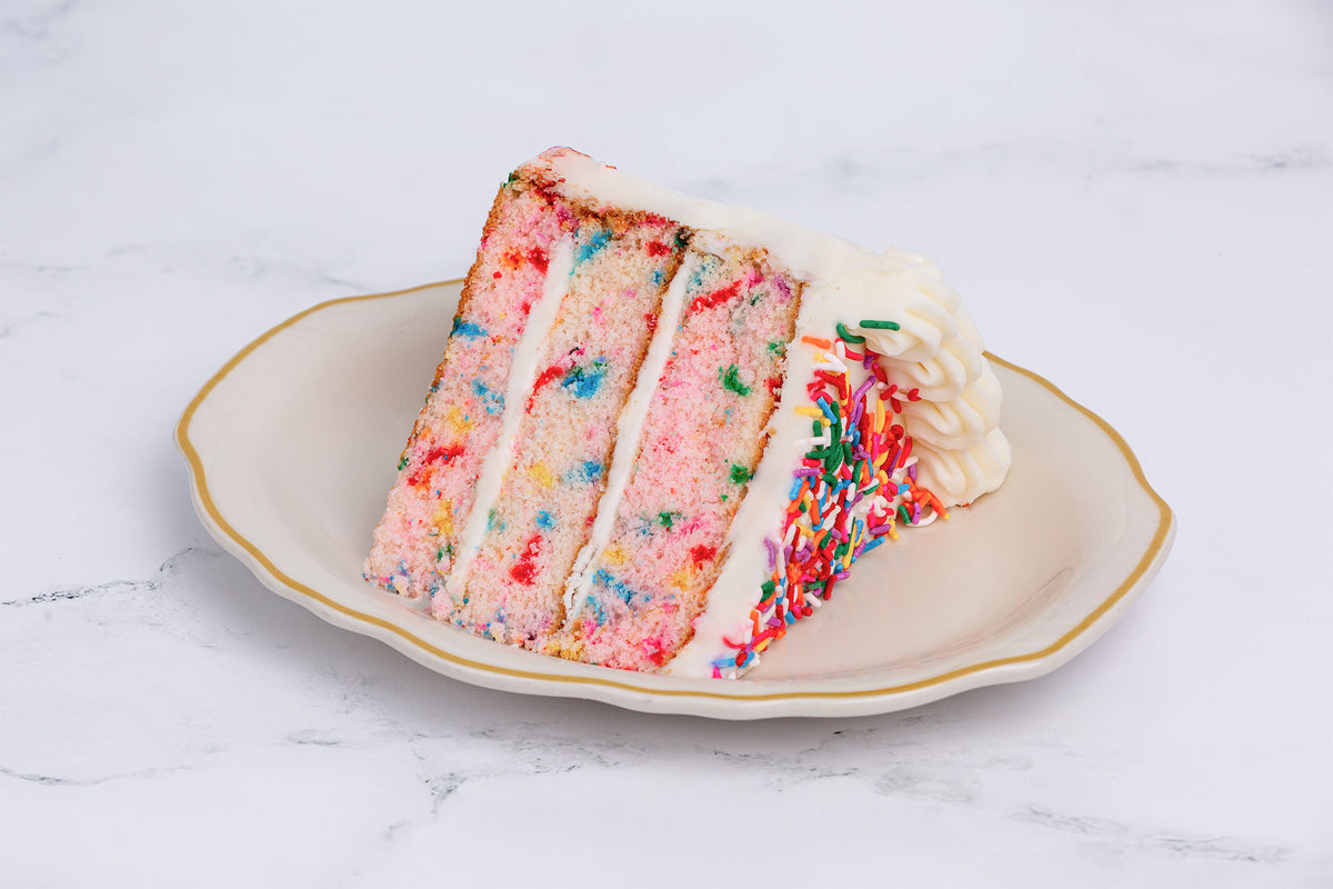 A slice of Winfield's confetti cake on a plate, sprinkles through the layers and buttercream between them