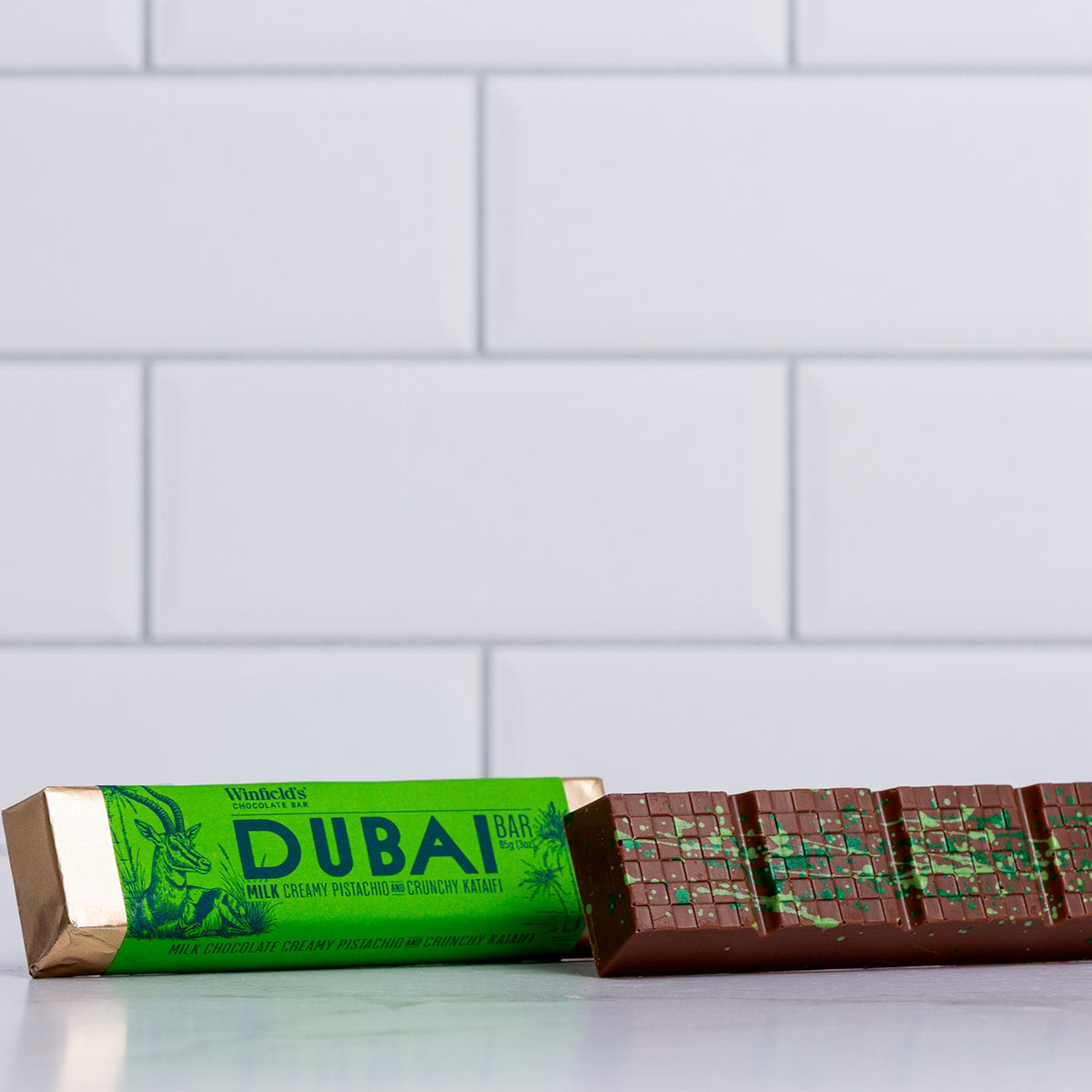 Winfield's Milk Chocolate Dubai Bar in its green wrapper beside the unwrapped bar showing the pistachio filling