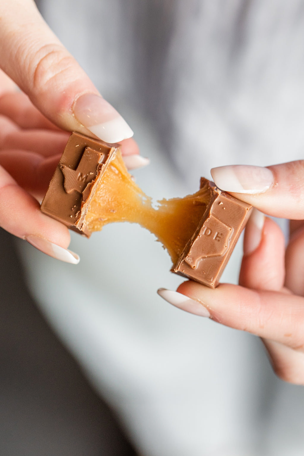 Hands pulling a Winfield's Texas-Made Caramel in half, the caramel centre stretching between the pieces