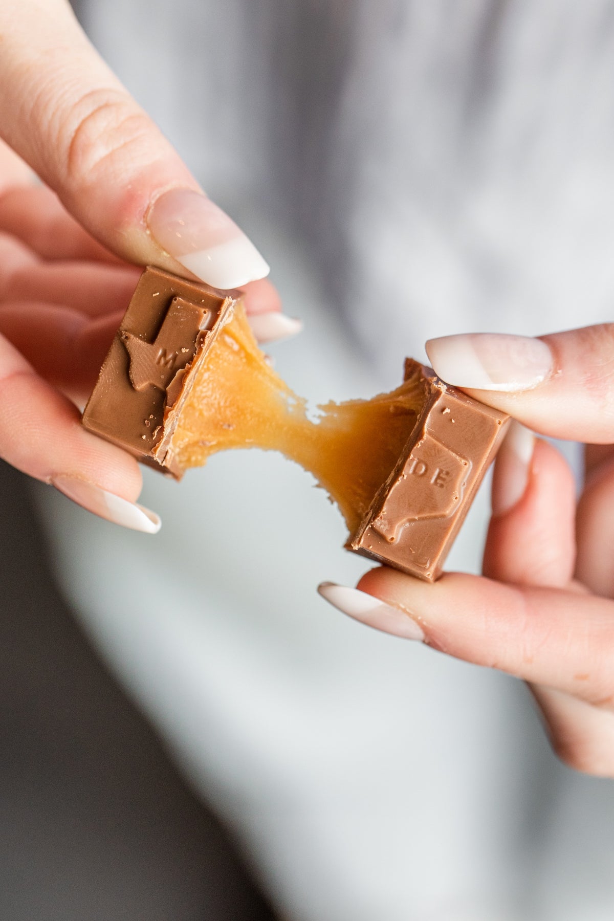 Hands pulling a Winfield's Texas-Made Caramel in half, the caramel centre stretching between the pieces