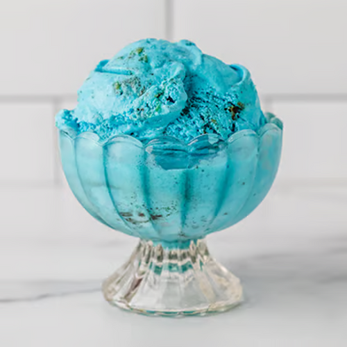 Scoops of Winfield's C is for Cookie ice cream, bright blue with cookie pieces, in a footed glass dish