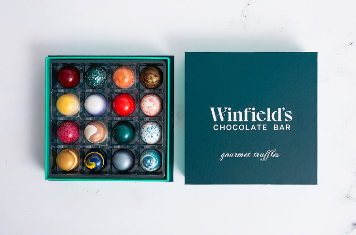 A sixteen-piece Winfield's truffle box open beside its teal gourmet truffles lid on a marble counter