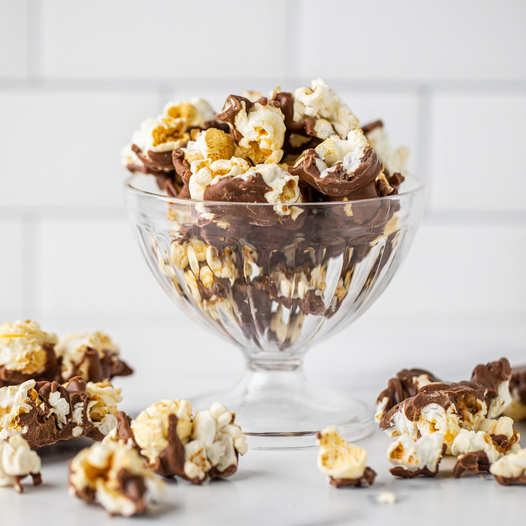 Winfield's milk chocolate popcorn piled in a footed glass dish, with pieces scattered alongside