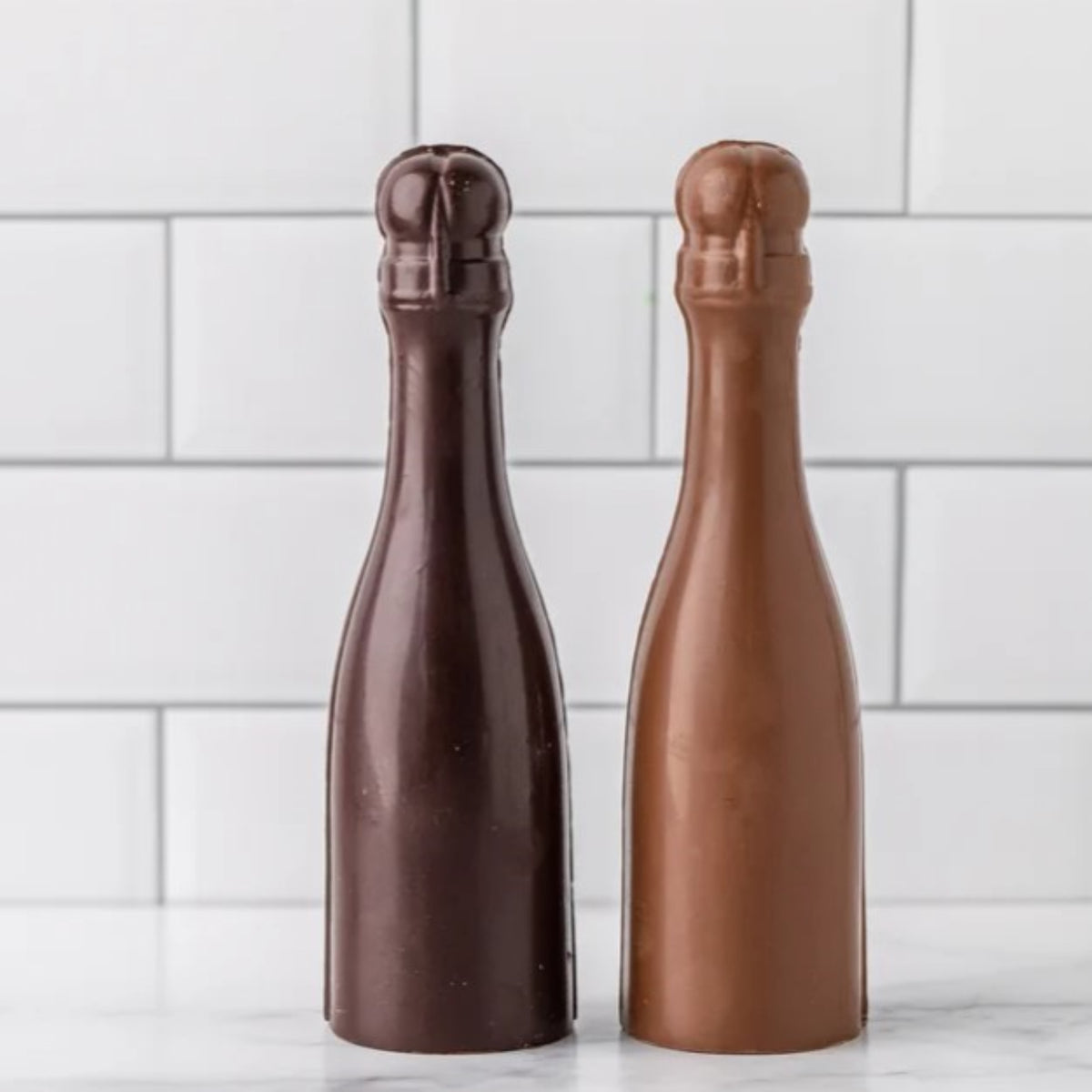 Two unwrapped Winfield's chocolate champagne bottles in dark and milk chocolate, side by side
