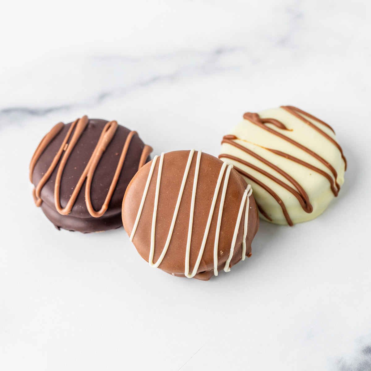 Three Winfield's chocolate-covered Oreos in dark, milk and white chocolate on marble